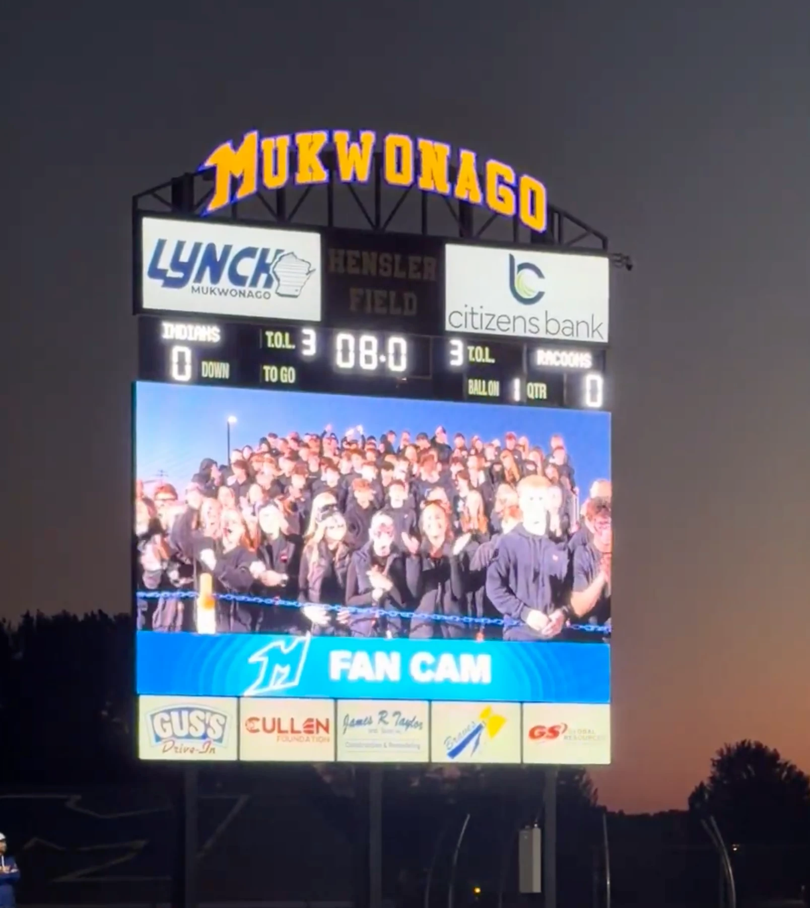 Mukwonago’s video board at dusk, showing the student section on the fan cam during a game